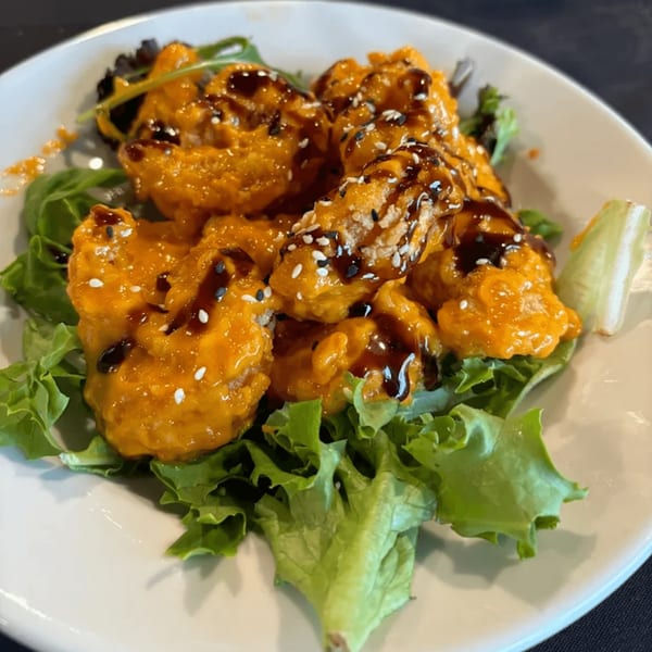Fried shrimp coated in orange sauce, drizzled with dark glaze and sesame seeds, on a bed of lettuce.