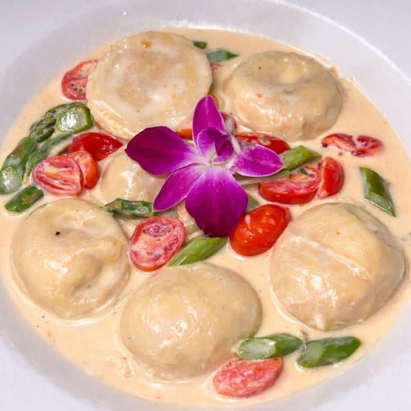 Italian ravioli in a creamy sauce with cherry tomatoes, green beans, and a purple orchid.
