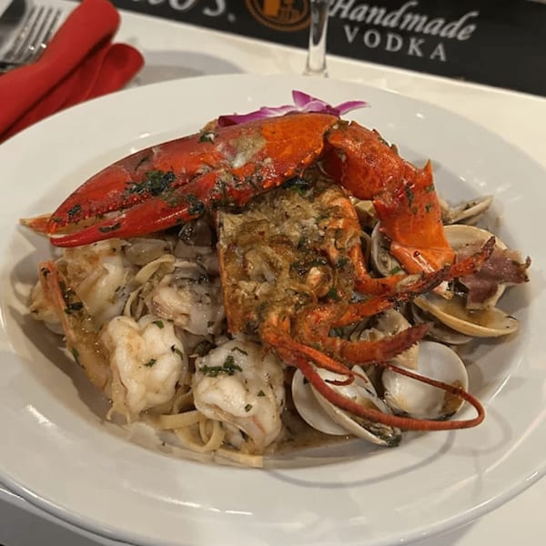 A large plate of Italian seafood pasta with a whole lobster, shrimp, and clams.