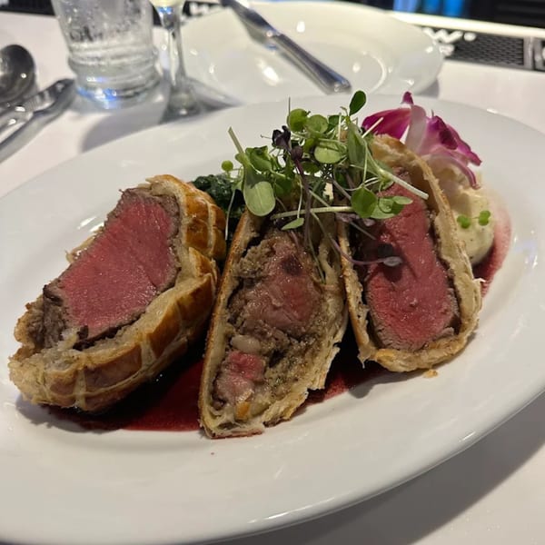 Three slices of beef Wellington with a red wine reduction, mashed potatoes, and microgreens.