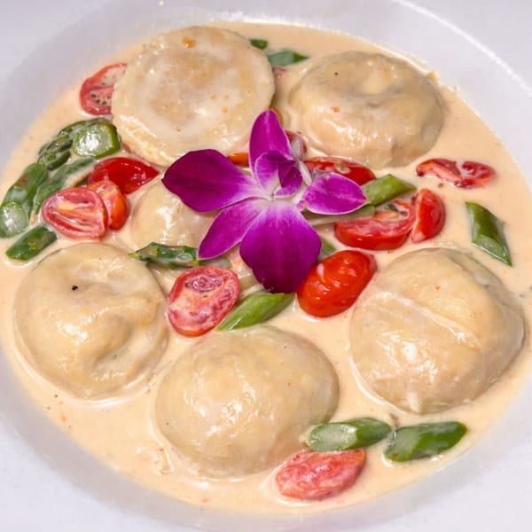 Italian ravioli in a creamy sauce with cherry tomatoes, green beans, and a purple orchid garnish.