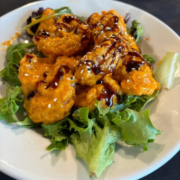 Crispy shrimp in orange sauce with sesame seeds and balsamic glaze on a bed of lettuce.