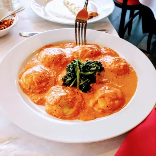 Ravioli in a creamy orange sauce with a dollop of spinach, a fork piercing one.