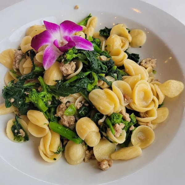 Orecchiette pasta with broccoli rabe, sausage, and a purple orchid garnish on a white plate.